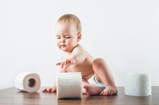 Bebé divertido y papel higiénico en la pared blanca. Niño rasgando papel higiénico. entrenamiento para ir al baño