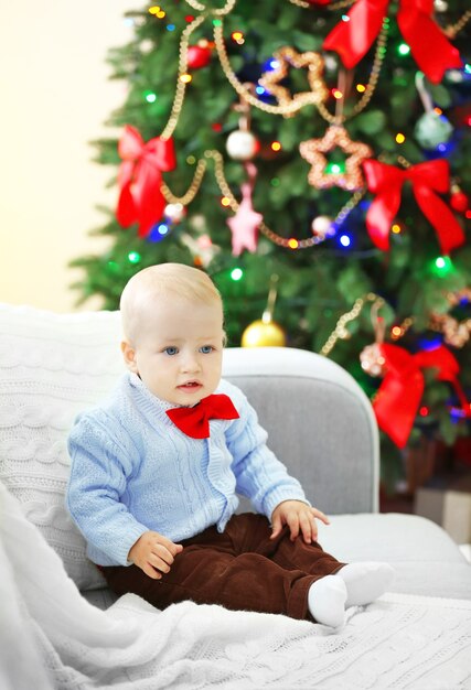 Bebé divertido sentado en el sofá y el árbol de Navidad en el fondo