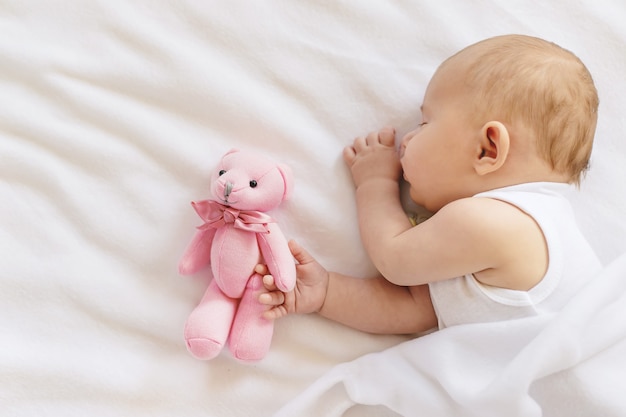 Bebê dorme com um ursinho de pelúcia em um fundo branco.