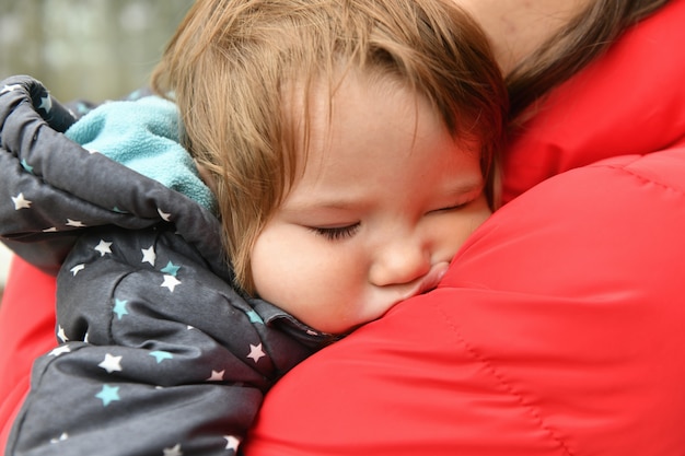 La bebé duerme en los brazos de su madre. despues de un paseo. De cerca. Bebé durmiendo. Bebé recién nacido duerme en brazos de su madre