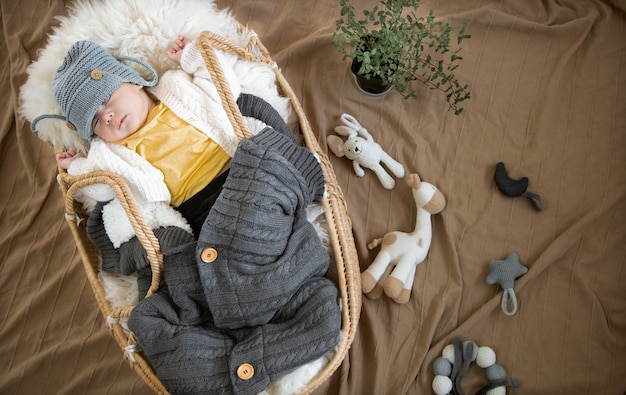 El bebé duerme dulcemente en una cuna de mimbre con un gorro de punto cálido y una manta cálida.