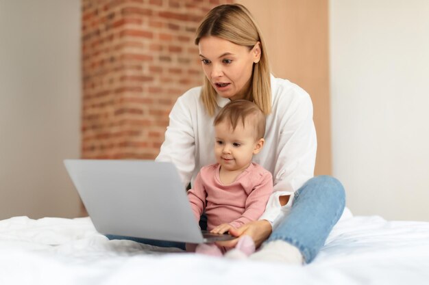 Bebê e gadgets mamãe e sua filhinha usando laptop navegando na internet para se divertir online