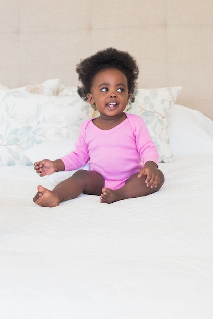 Foto bebé em babygro rosa sentado na cama