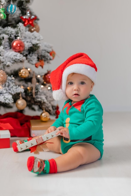 bebê em traje de gnomo de Natal abre presentes perto de produtos de árvore de Natal para crianças e feriados