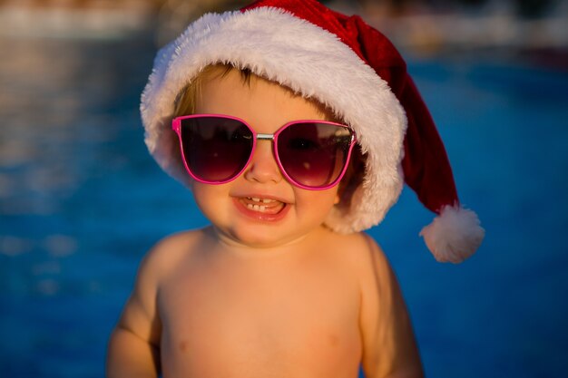 Bebê em um chapéu de papai noel e óculos de sol na piscina