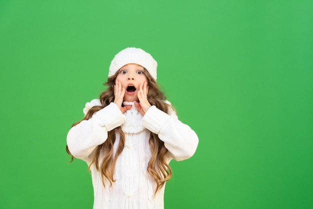 Bebê em um suéter quente e um gorro de malha fica muito surpreso e levou as mãos à boca aberta. Uma criança com cabelo bonito em roupas quentes de inverno.