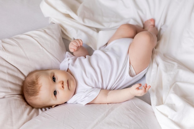 Bebê em uma roupa branca está deitado de costas em uma cama feita com roupa de cama branca. sono e descanso das crianças. conceito de uma infância feliz e maternidade. estilo de vida, espaço para texto. foto de alta qualidade