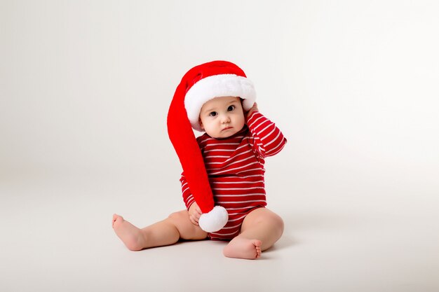 bebê em uma roupa vermelha e chapéu de Papai Noel em uma parede branca