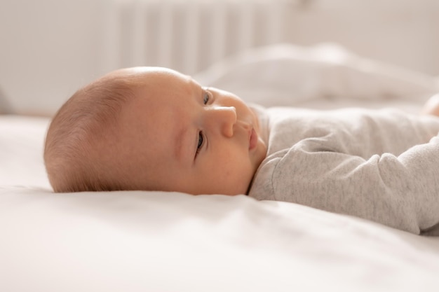 Bebê encantador com olhos azuis em uma roupa branca está na parte de trás do estilo de vida de roupa de cama branca