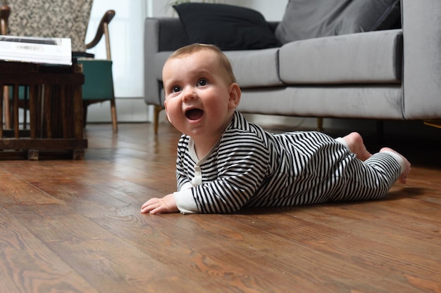 Bebê engatinhando no chão de casa, com piso de madeira olhando para cima