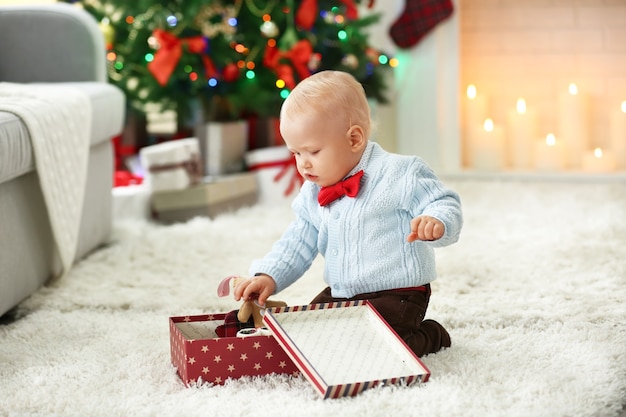 Bebê engraçado com caixa de presente, árvore de Natal e lareira no fundo