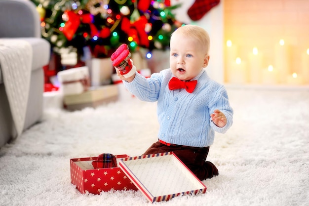 Bebê engraçado com caixa de presente, árvore de Natal e lareira no fundo