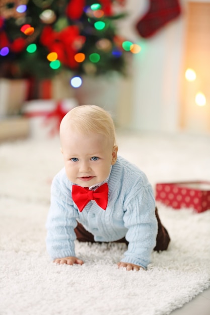 Bebê engraçado com caixa de presente, árvore de Natal e lareira