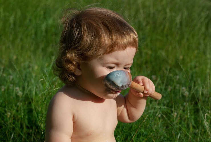 Foto bebê engraçado no parque se come com uma colher de madeira grande fundo da natureza desfocado alimentação saudável para crianças nutrição infantil