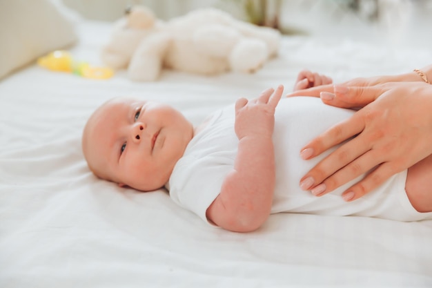 El bebé está acostado en la cama durante 2 meses la mano de la madre sobre el estómago del bebé bebé recién nacido