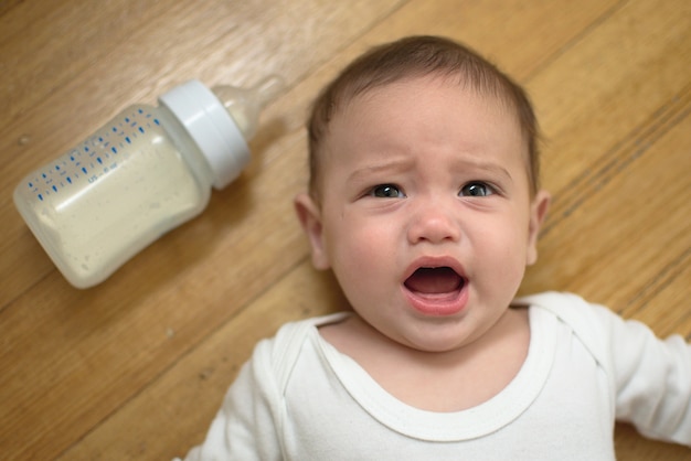 Foto bebê está chorando no chão com a garrafa de fórmula