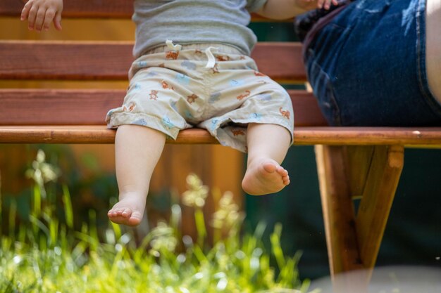 El bebé está sentado en un banco del parque con los pies descalzos cerca del horario de verano