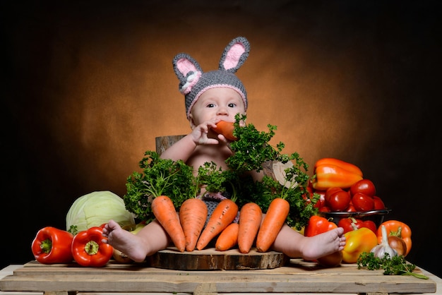 Bebê fantasiado de coelho com legumes em uma madeira