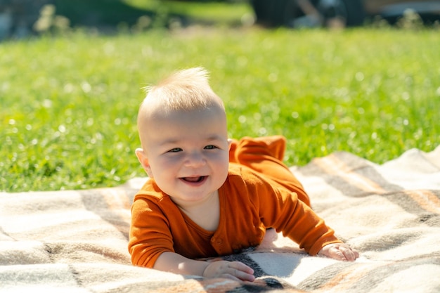 Bebé feliz acostado en la manta en la hierba soleada
