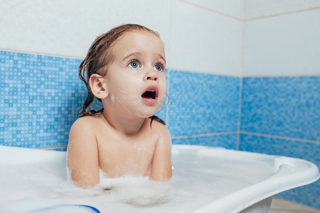 El bebé feliz alegre del niño de la diversión que toma un baño que juega con espuma burbujea.