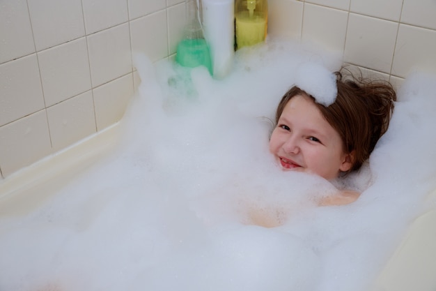 Bebé feliz en el baño, nadando en la ducha de espuma.