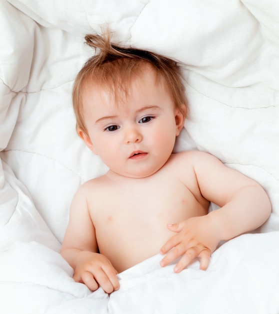 Bebê feliz de 11 meses deitado em um cobertor branco e sorrindo