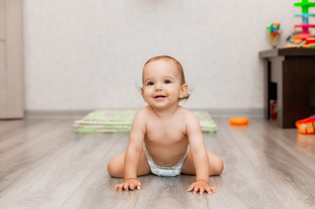 Bebê feliz de 11 meses rasteja no chão e ri. a criança está sentada no chão.