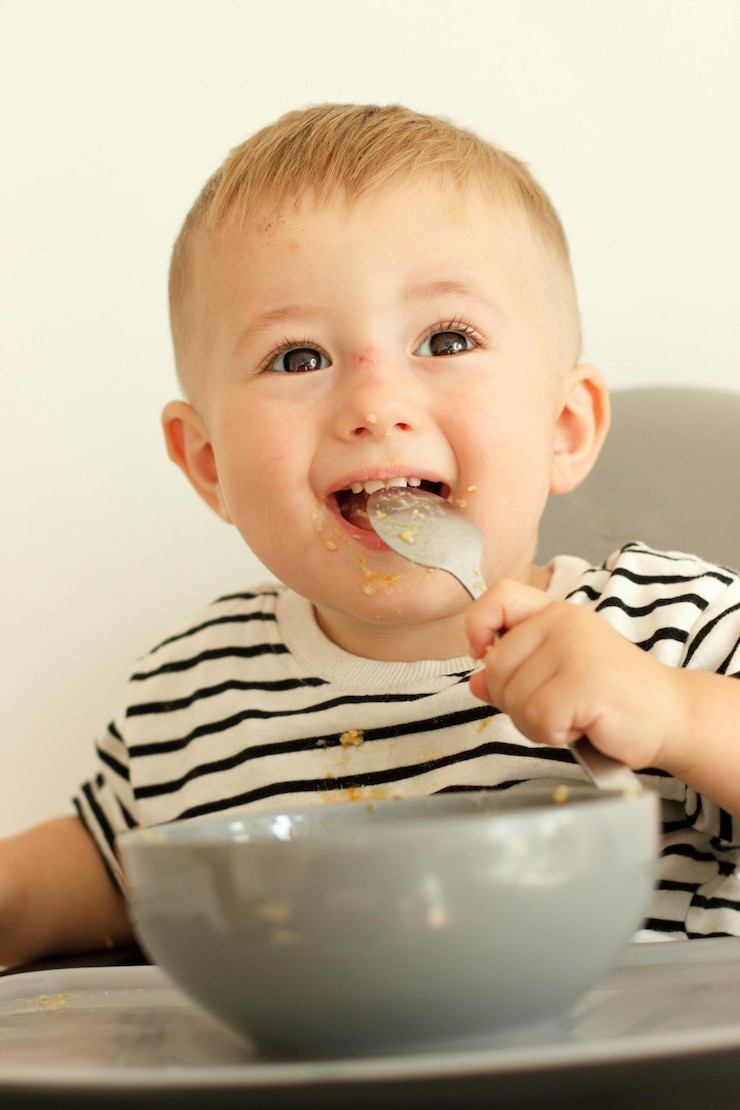 Foto un bebé feliz está comiendo comida con una cuchara en la boca