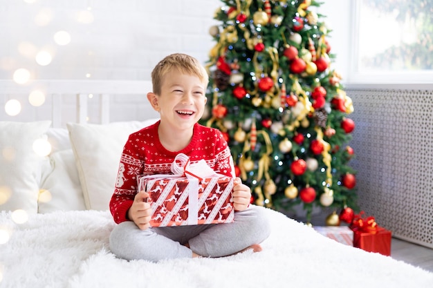 El bebé feliz está contento con los regalos, los niños están en casa para las vacaciones de Navidad. Vacaciones de año nuevo. El niño está en una habitación decorada de forma festiva con un árbol de Navidad. Retrato de un niño