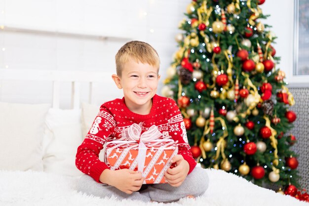 El bebé feliz está contento con los regalos, los niños están en casa para las vacaciones de Navidad. Vacaciones de año nuevo. El niño está en una habitación decorada de forma festiva con un árbol de Navidad. Retrato de un niño