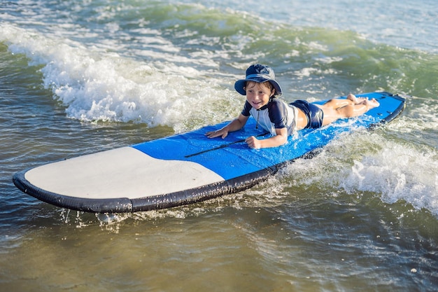 Bebé feliz - paseo joven surfista en tabla de surf con diversión en las olas del mar. Estilo de vida familiar activo, clases de deportes acuáticos al aire libre para niños y actividad de natación en el campamento de surf. Vacaciones de verano con niño