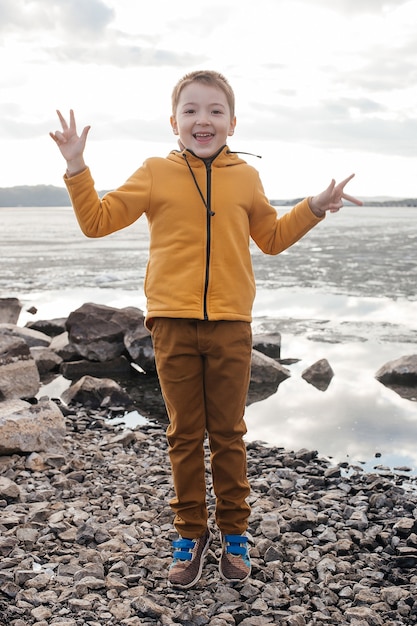 Foto bebé feliz saltando en la orilla del río. el niño se está divirtiendo y sonriendo. naturaleza y recreación.