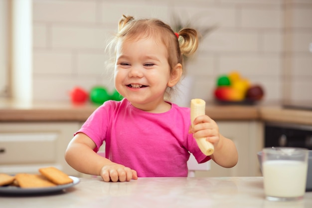 Bebê feliz sentado à mesa da cozinha e comendo com apetite