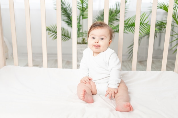 Bebê feliz sentado em um berço com uma roupa branca