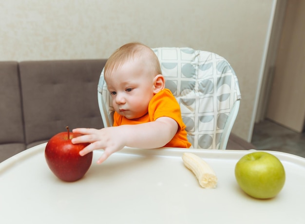 Bebé feliz sentado en una silla alta comiendo manzanas