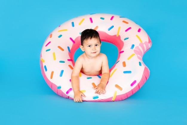 Bebé feliz en traje de baño con anillo de natación donut en una pared azul de color