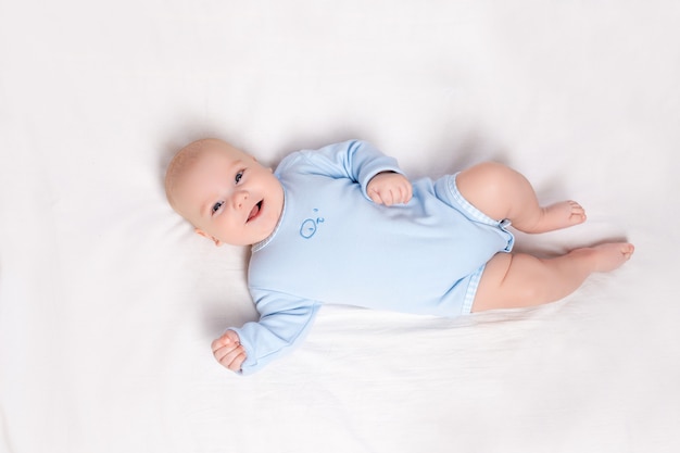 Bebé feliz yace en la cuna, lindo niño de seis meses se encuentra en la cama de la guardería