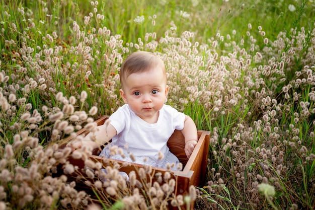 Bebé en flores en el campo en verano con un vestido blanco