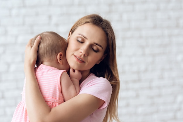 Bebê fofo abraçando com alegre jovem mãe.