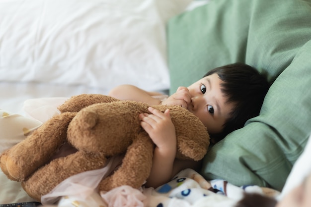 Bebê fofo abraçando o ursinho de pelúcia e dormindo na cama