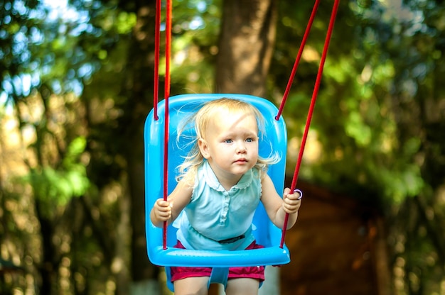 bebê fofo balançando no parque com árvores altas e raios de sol passando