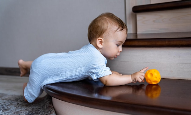 Bebê fofo brincando com bola na escada Menino brincando com brinquedo colorido Hall de entrada e interior da sala de estar Segurança em casa para crianças