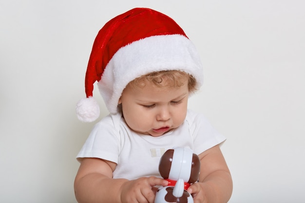 Bebê fofo com chapéu de natal e camiseta brincando com o brinquedo favorito isolado no espaço em branco