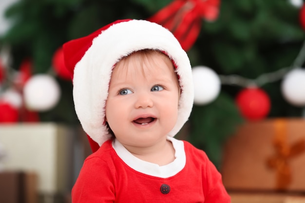 Bebê fofo com chapéu de papai noel contra um fundo desfocado de natal