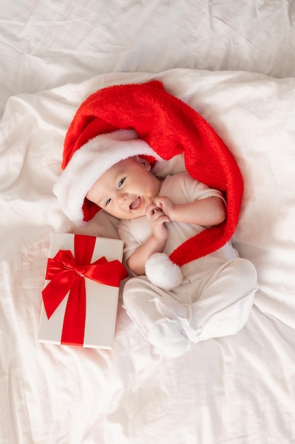 bebê fofo com chapéu de Papai Noel em casa na cama. O primeiro ano novo. Presente de Natal