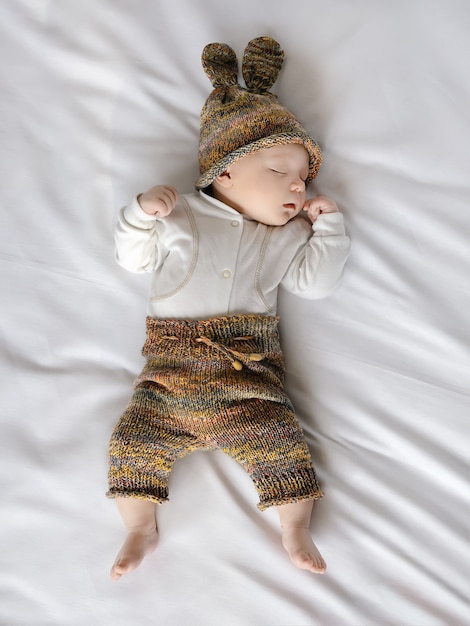 Bebê fofo com gorro e shorts dormindo no lençol branco, dia do bebê, mãe e família