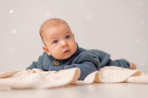 Bebê fofo com olhos azuis em macacão de malha azul encontra-se em sua barriga em fundo sólido xadrez cinza