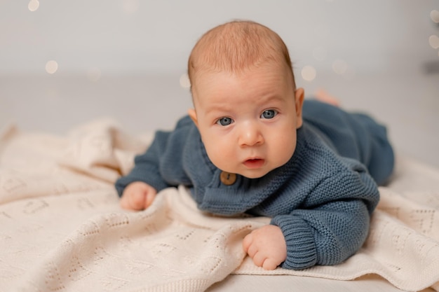 Bebê fofo com olhos azuis em macacão de malha azul encontra-se na barriga na manta cinza. criança aprende a engatinhar. maternidade e infância. histórico sólido. espaço para texto. Foto de alta qualidade