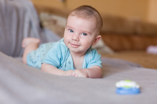 Bebê fofo com roupas azuis, deitado no sofá e sorrindo.