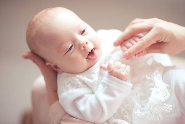 Bebé fofo com um vestido branco deitado nas mãos da mãe
